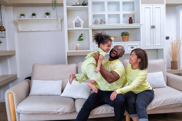 Young family with small daughter sitting on sofa playing and laughing together in the living room