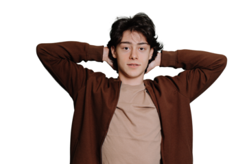Handsome caucasian brunet teen boy in brown sweater standing against transparent background looks at camera putting hands on back of head. Italian guy, student laying, top view.