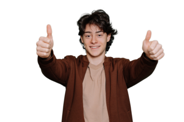 Handsome brunet Spanish boy in brown jacket and beige t-shirt smiles wide shows thumb up gesture by both hands looks at camera stands against transparent background. Excited teen guy toothy smiles.