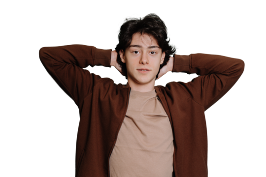Handsome caucasian brunet teen boy in brown sweater standing against transparent background looks at camera putting hands on back of head. Italian guy, student laying, top view.