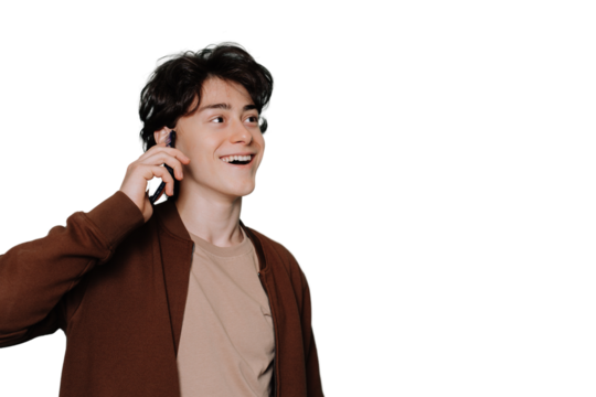 Amazed young handsome guy in beige t-shirt and brown jacket talks by phone toothy smiles looks aside standing against transparent background. Brunette boy isolated with copy space for ad. Mockup. - Powered by Adobe