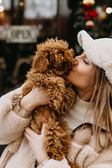 Closeup of a young woman holding a puppy, kissing him, outdoors