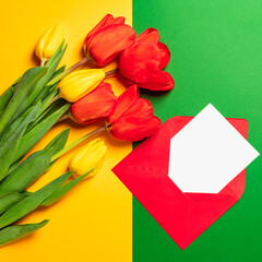 Fototapeta premium Bouquet of red and yellow tulips and a red envelope and an empty blank. Greeting card for Mother's Day, International Women's Day, Valentine's Day and Easter. Spring holidays.