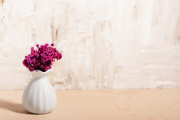 Small ceramic vase with dried flowers on a wooden table.