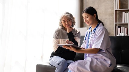 Fototapeta premium Nurse talking with a nursing home patient about his health. The nurse is making notes on a digital tablet