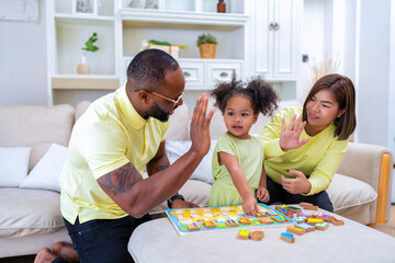 Obraz premium Young family with small daughter sitting on sofa playing arrange alphabet in the living room