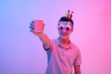 A young party animal raises his cup of punch. Wearing hilarious birthday novelty shades and having...