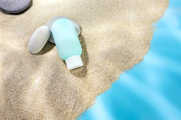 Sunscreen in a plastic tube on a background of sand with stones and light effects