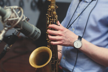 View of a saxophone player in headphones during rehearsal, recording sound for new album song at...