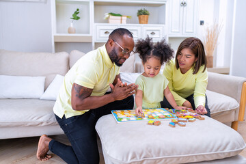 Young family with small daughter sitting on sofa playing arrange alphabet in the living room