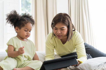 Fototapeta premium Asian mother teach daughter using digital tablet at home. Asian family spending time together at home. Education and technology concept