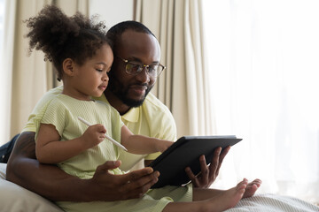 African American father teach daughter using digital tablet at home. African American family spending time together at home. Education and technology concept - Powered by Adobe