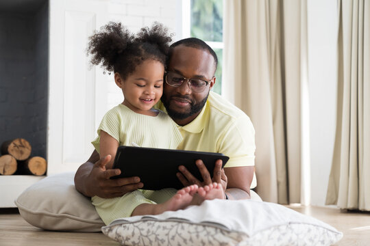 African American father teach daughter using digital tablet at home. African American family spending time together at home. Education and technology concept