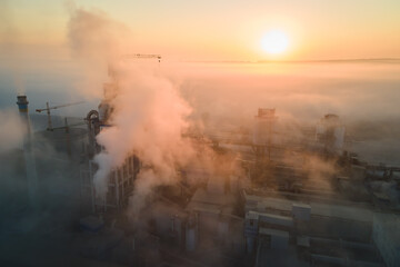 Fototapeta premium Aerial view of cement factory with high concrete plant structure and tower crane at industrial production site on foggy morning. Manufacture and global industry concept