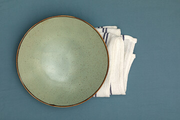 Green bowl on the white fabric napkin. Blue fabric backdrop.