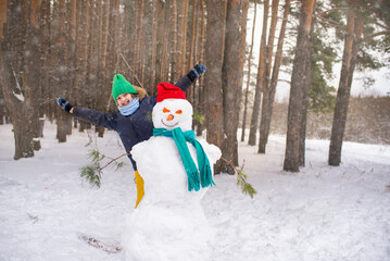 a boy peeks out from behind a snowman, a happy child plays hide and seek in the winter forest	