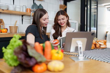 Beautiful woman and friend talking and using laptop at kitchen room. Girl friends couple living...