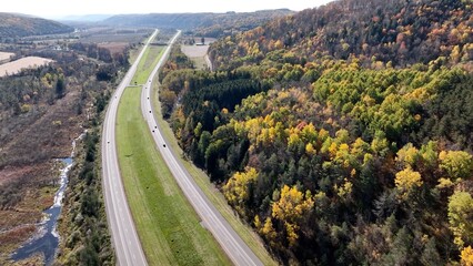 Fototapeta premium Cars traveling across American on road trip on highway roads through beautiful countryside during Autumn season with Fall colors in trees and landscape