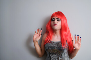 Fototapeta premium Portrait of transgender man dancing and wearing a red wig on grey background. LGBTQ queer.
