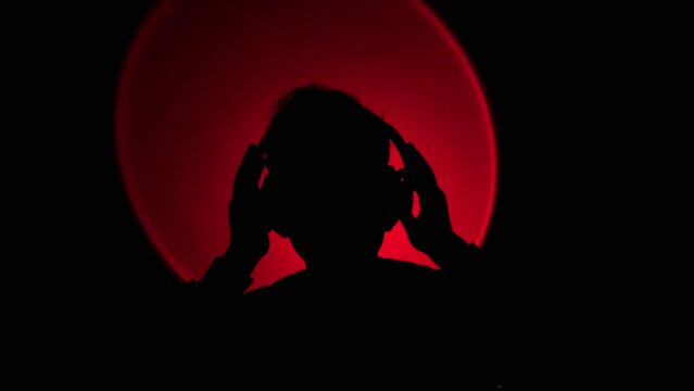 male listening to music with headphones in the dark with red backlight