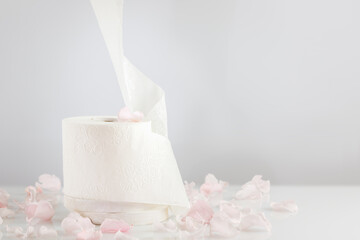 Roll of natural white toilet paper on a light background with rose petals. White toilet tissue, Hygiene product. Restroom soft touch toilet paper. Soft focus style image. Front view, copy space