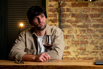 Sad man complains and drinks wine alone at home. Drunk man drinks a glass of red wine.