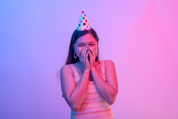 A young female birthday celebrant wearing a party hat blushes with happiness. Lit with blue and...