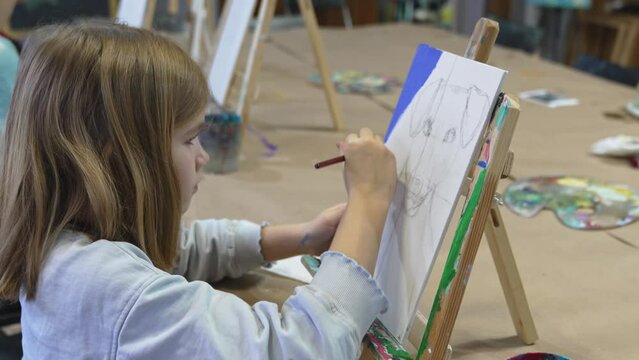 a little girl mpaints with acrylic paints a painting on canvas in an art studio