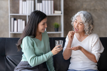 Asian elderly woman taking medicine for her ailments in the living room at home under the close supervision of her daughter.