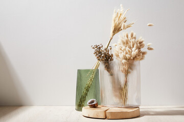 green and white glass vase with dry flowers stand on a wooden stand, wooden desk, background white wall