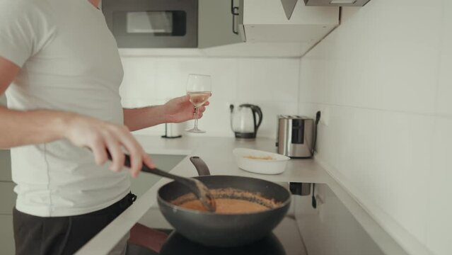 junger Mann tanzt in der modernen K&uuml;che beim kochen und Wein trinken