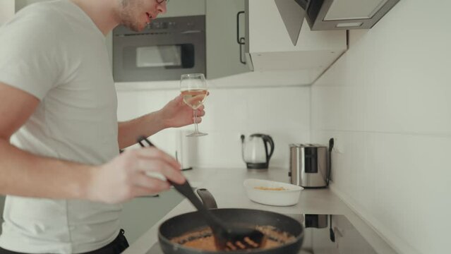 junger Mann tanzt in der K&uuml;che beim zubereiten eines Auflaufes und trinkt wein