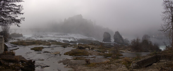 Wide angle view of scenic landscape with rock and castle on a hill at Rhine Falls on a foggy winter morning. Photo taken February 16th, 2023, Neuhausen am Rheinfall, Switzerland.