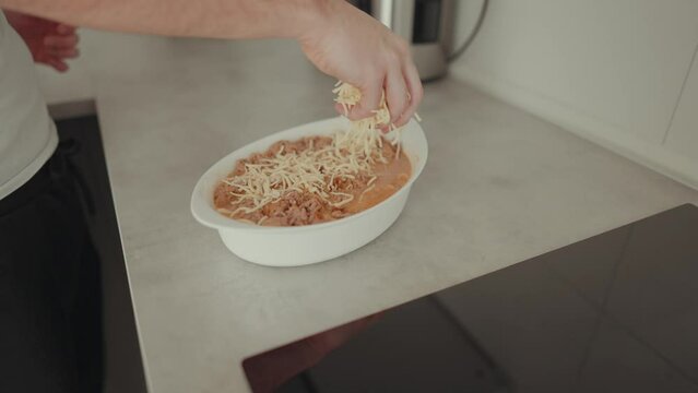 junger Mann der Gouda / Geriebenen K&auml;se &uuml;ber einen Auflauf streut