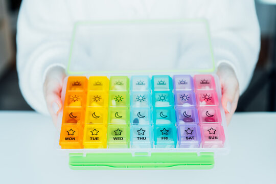 Close up Female hands holding opened weekly pills organizer. Taking daily medicine antioxidant diet vitamin supplements for beauty skin hair health care medicament biohacking concept. Selective focus.