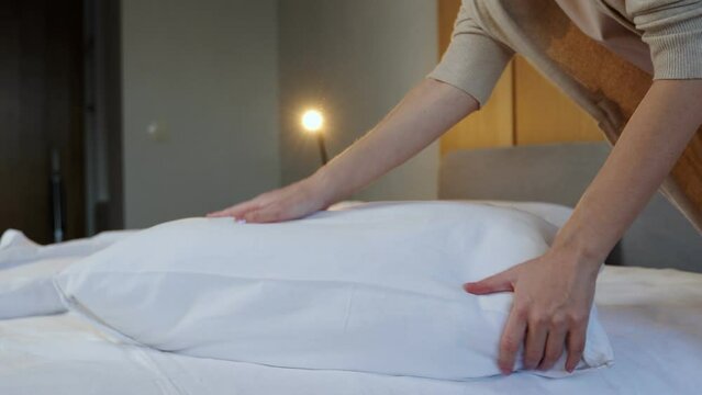 Woman fluffing soft pillow in bedroom. Woman with her hands fluffs up a pillow lying on the bed. 