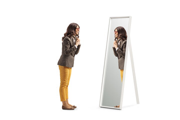 Full length profile shot of a young woman getting ready in front of a mirror and putting a scarf - obrazy, fototapety, plakaty