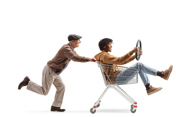 Elderly caucasian man pushing an african american guy inside a shopping cart