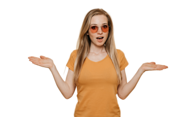 Shocked young red haired woman in sunglasses, dressed in orange t-shirt, spreads her hands in surprise, making choice, posing over transparent background. People sincere emotions.