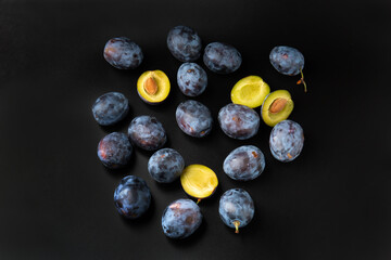 Blue plums on a black background with water drops top view.