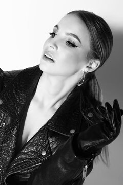 Fashion and make-up concept. Beautiful woman studio portrait with black punk leather jacket and classical hairstyle. Model without bra looking aside the camera. Black and white image