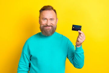 Photo of rich confident man wear trendy clothes demonstrates recommend plastic card bank easy payment isolated on yellow color background