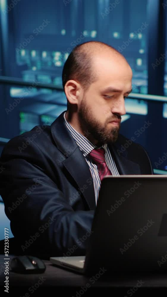 Poster vertical video: male infrastructure engineer working in render farm running diagnostics on mainframe