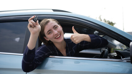 Happy female client smiling and gesturing thumb up while sitting in new vehicle and Showing key.
