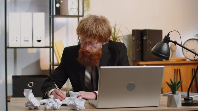 Angry furious young man working at office throwing crumpled paper, having nervous breakdown at work, migaine, headache, stress management, mental distress problems, losing temper, reaction on failure