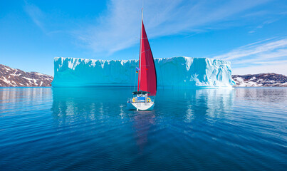 Melting icebergs by the coast of Greenland, on a beautiful summer day - Melting of a iceberg and pouring water into the sea with lone yacht - Greenland  
