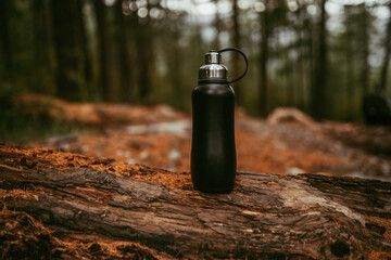Black metal thermo bottle in the forest