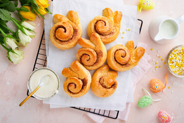 Easter breakfast Holliday concept. Easter bunny buns rolls with cinnamon made from yeast dough with orange glaze, easter decorations, colored eggs on pink spring background. Easter Holliday card.
