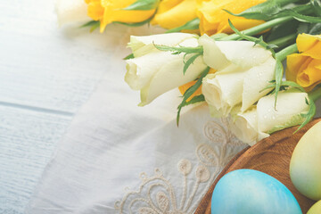 Fototapeta na wymiar Happy Easter. Easter eggs on rustic table with white and yellow roses. Natural dyed colorful eggs in wooden plate and spring flowers in rustic room. Toned image. Easter background with copy space.