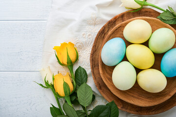 Obraz na płótnie Canvas Happy Easter. Easter eggs on rustic table with white and yellow roses. Natural dyed colorful eggs in wooden plate and spring flowers in rustic room. Toned image. Easter background with copy space.